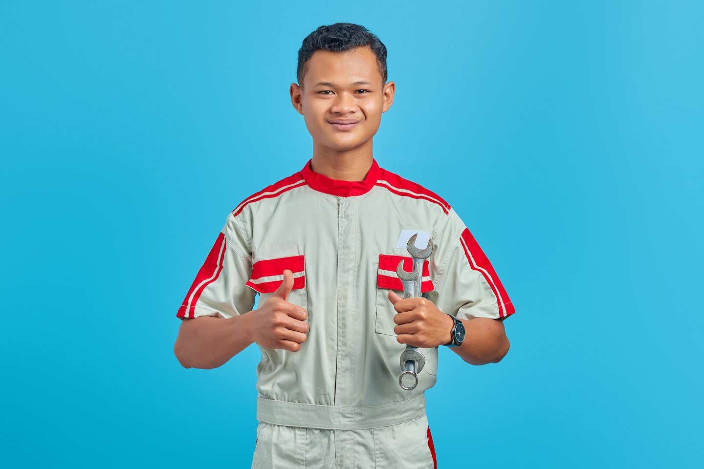 Male technician in uniform gives a thumbs up holding a wrench.